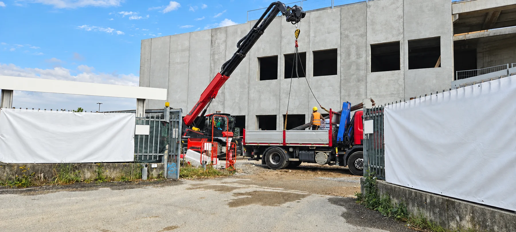 Foto reale ritoccata: mezzi di sollevamento e un operatore all’ingresso di un’area di cantiere.